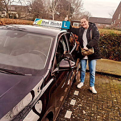 Geslaagde leerling met duim omhoog bij de lesauto